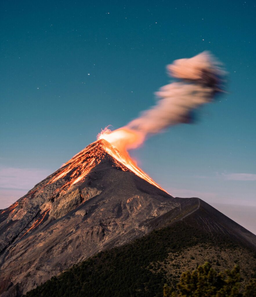 Rauchender Vulkan, im Hintergrund ist ein mittelblauer Sternenhimmel zu sehen