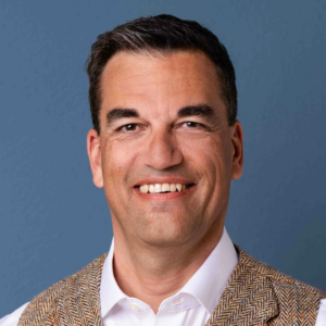 Portrait von Christian Bähner, Moderator beim GFK-Onlinekongress 2026. Freundlicher Ausdruck, aufgenommen vor einem blauen Studiohintergrund.