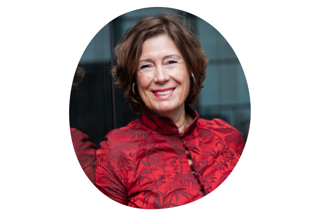 Person trägt eine rote, gemusterte Bluse mit asiatisch inspiriertem Stehkragen und Knopfleiste. Im Hintergrund ist eine spiegelnde Glasfläche zu sehen.