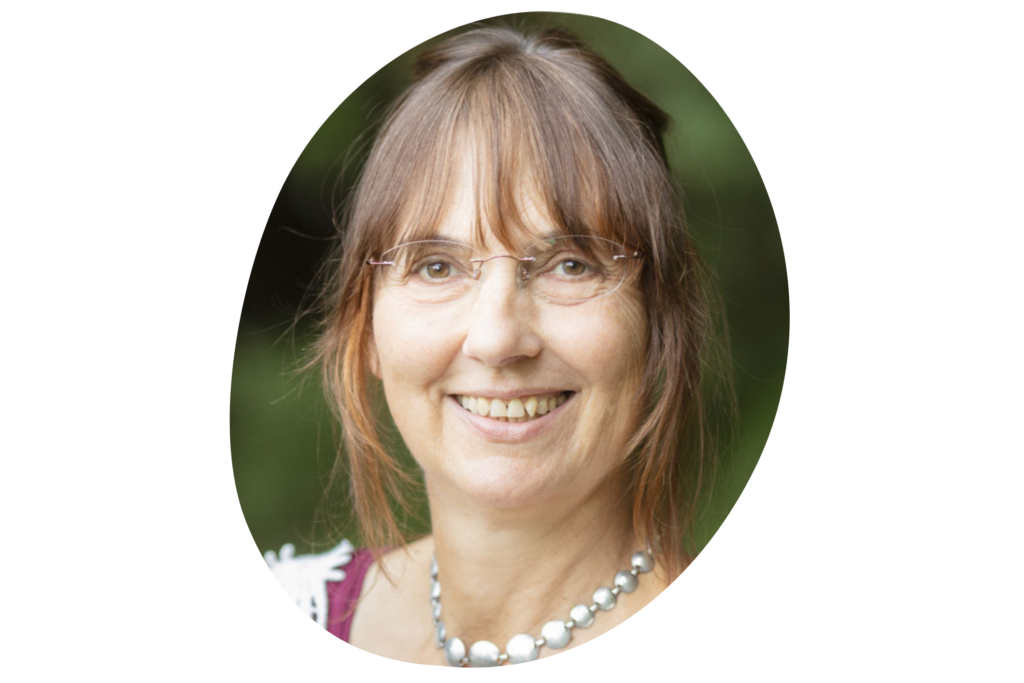 Nahaufnahme des Gesichts einer Frau, die braune Haare hat, eine Brille und auffällige Perlenkette trägt.