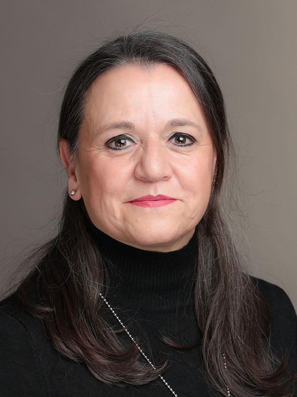 Frau mit langen dunklen Haaren in schwarzem Rollkragenpullover vor grauem Hintergrund.