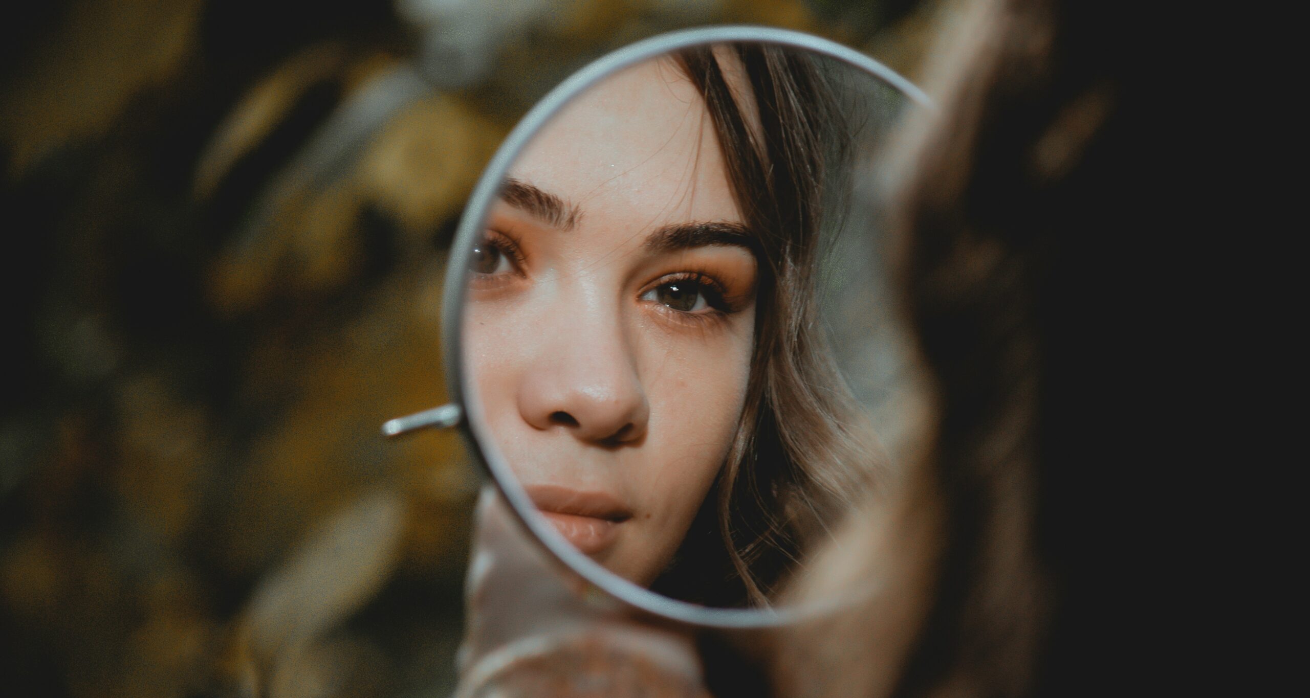 Ansicht einer Frau, die sich durch einen Handspiegel ansieht.