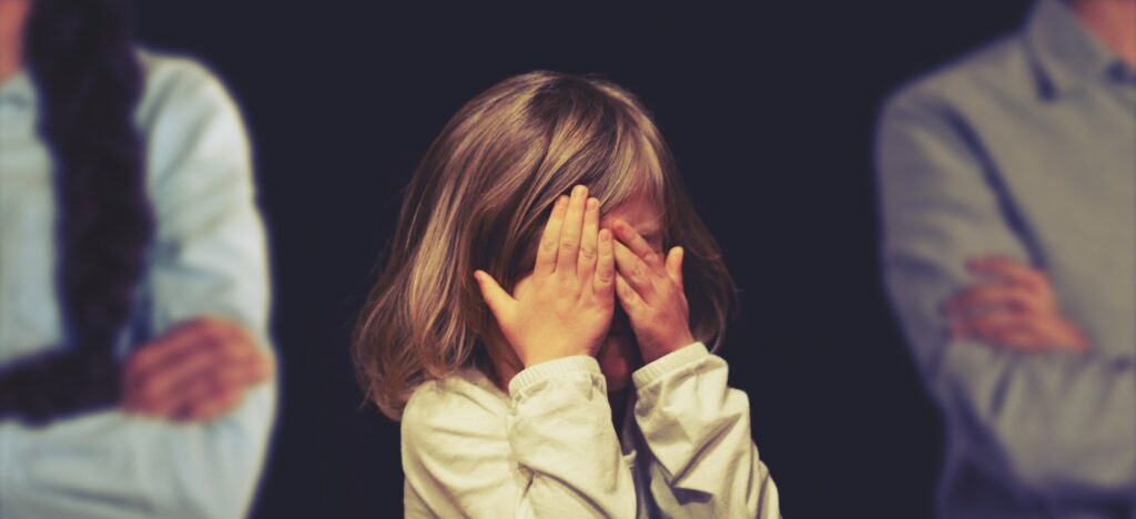 Kind, das zwischen Eltern steht und sich die Augen zuhält