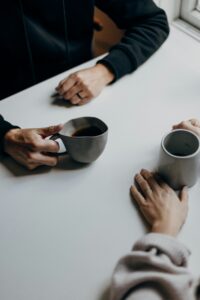 Die Hände von zwei Personen, auf einem Tisch mit Kaffeetassen.