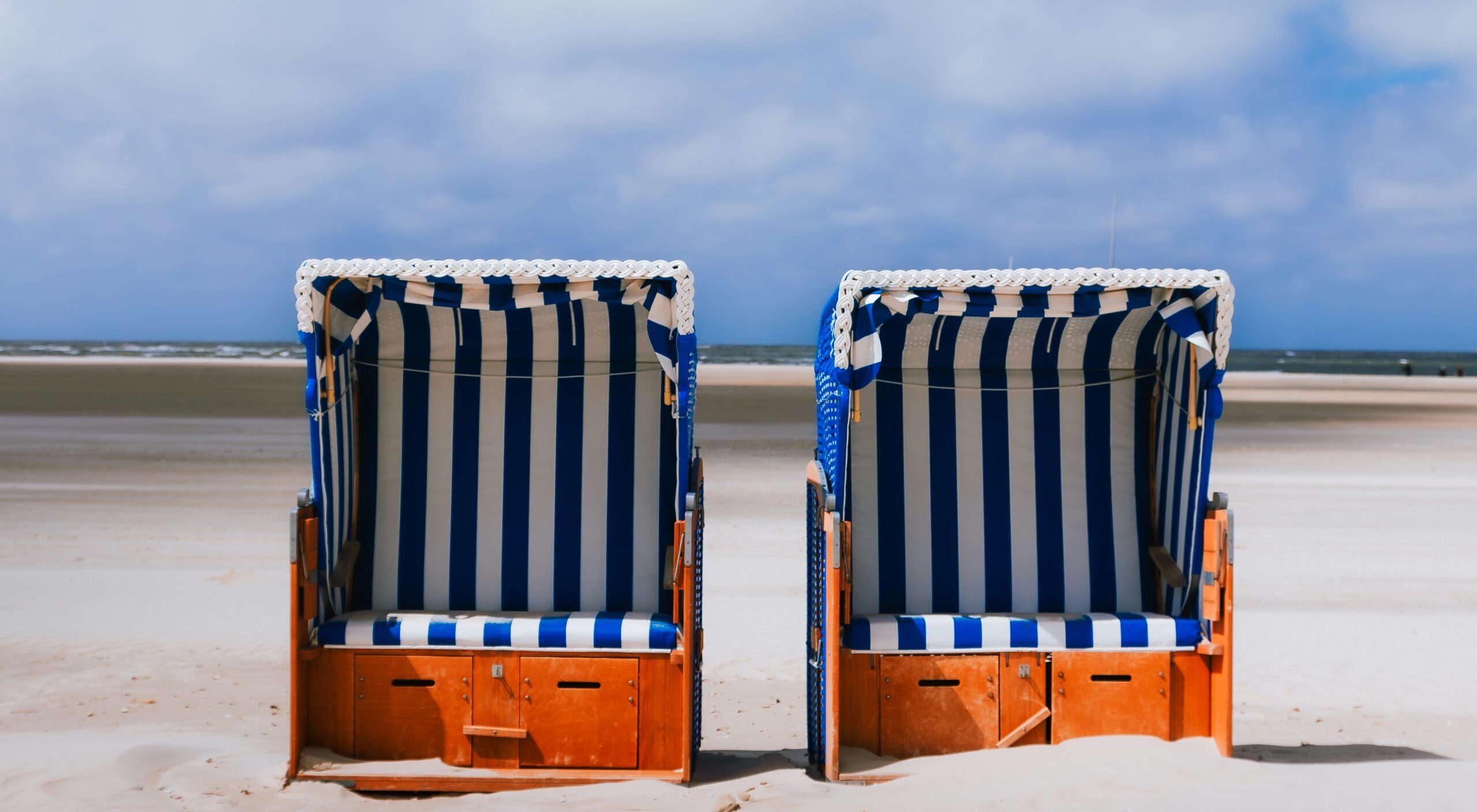 Zwei blauweiß gestreifte Strandkörbe auf Sand stehend, am Meer