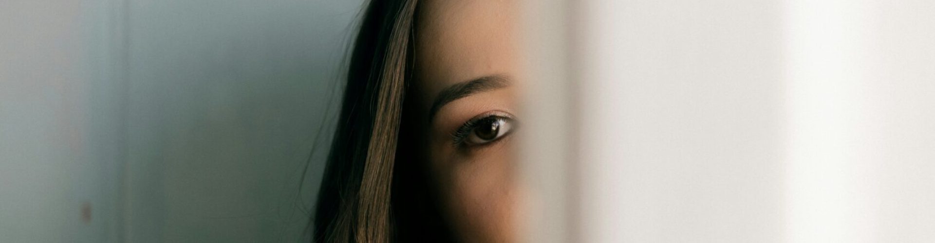 erson blickt mit einem Auge durch einen schmalen Türspalt in einem hellen Innenraum.
