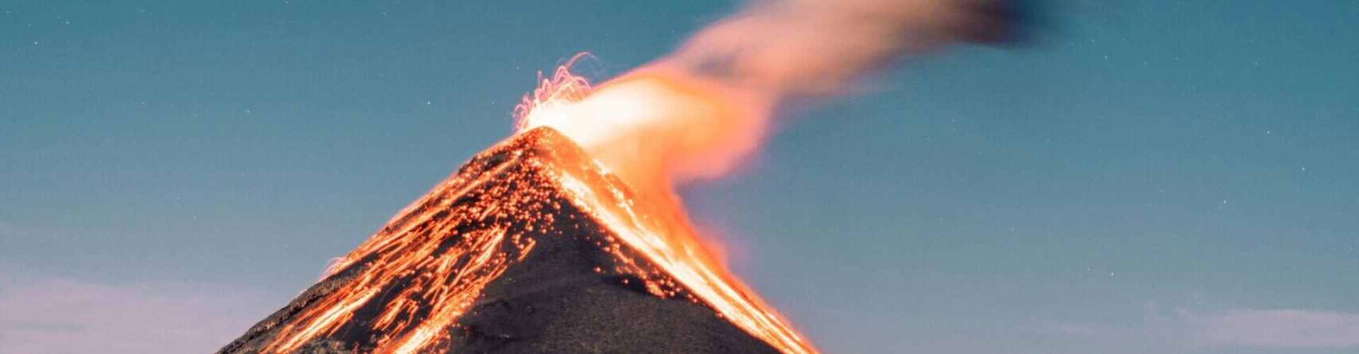 Rauchender Vulkan, im Hintergrund ist ein mittelblauer Sternenhimmel zu sehen