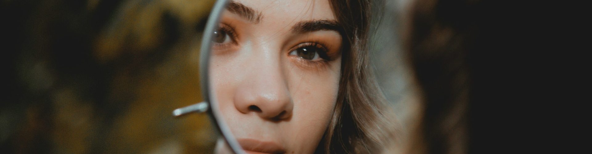 Ansicht einer Frau, die sich durch einen Handspiegel ansieht.