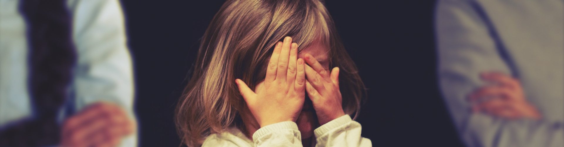 Kind, das zwischen Eltern steht und sich die Augen zuhält