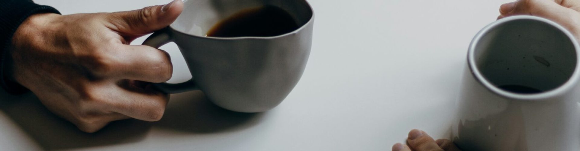 Die Hände von zwei Personen, auf einem Tisch mit Kaffeetassen.