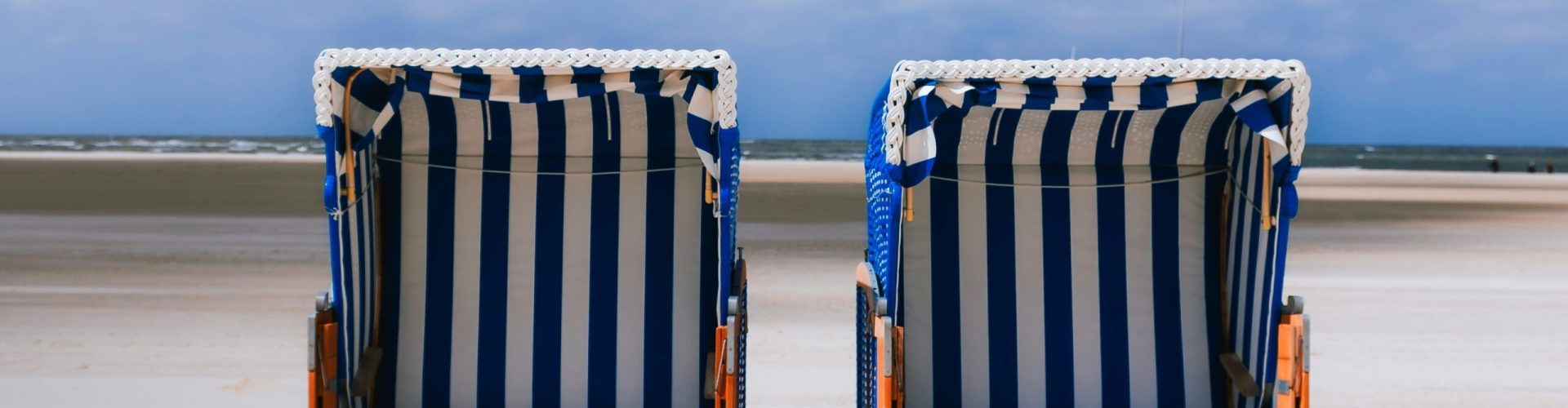 Zwei blauweiß gestreifte Strandkörbe auf Sand stehend, am Meer